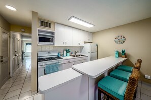 A kitchen with white cabinets, a stove, a refrigerator, and a clock on the wall. - Crystal Blue Persuasion - 1BR condo right on Sapphire Beach, sleeps 4! (St. Thomas)