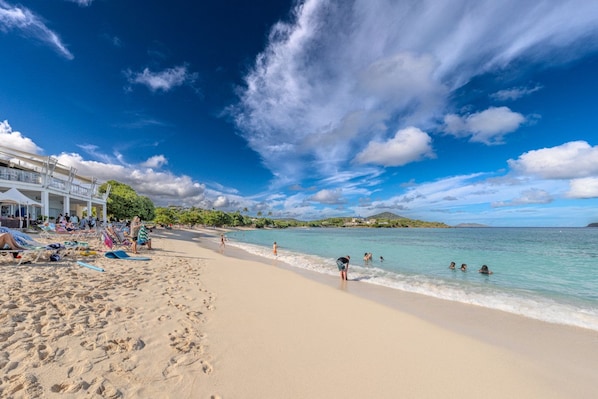 A beach with sun loungers and umbrellas, a building with a balcony, and a clear view of the sea. - Crystal Blue Persuasion - 1BR condo right on Sapphire Beach, sleeps 4! (St. Thomas)