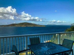 Un balcon avec une table et des chaises donnant sur une étendue d’eau et une île lointaine.