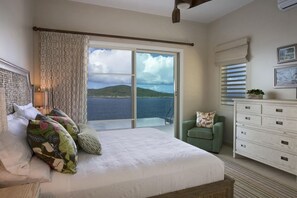 A bedroom with a large bed, a green armchair, a white dresser, and a view of the sea through a sliding glass door. - Luxury Villa with Infinity Pool Near Magens Bay (St. Thomas)
