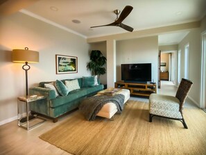 A living room with a green sofa, a TV, a ceiling fan, and a large plant. - Cliff-side 5BR villa - stunning down-island views & 5 mins from Magen`s Bay! (St. Thomas)