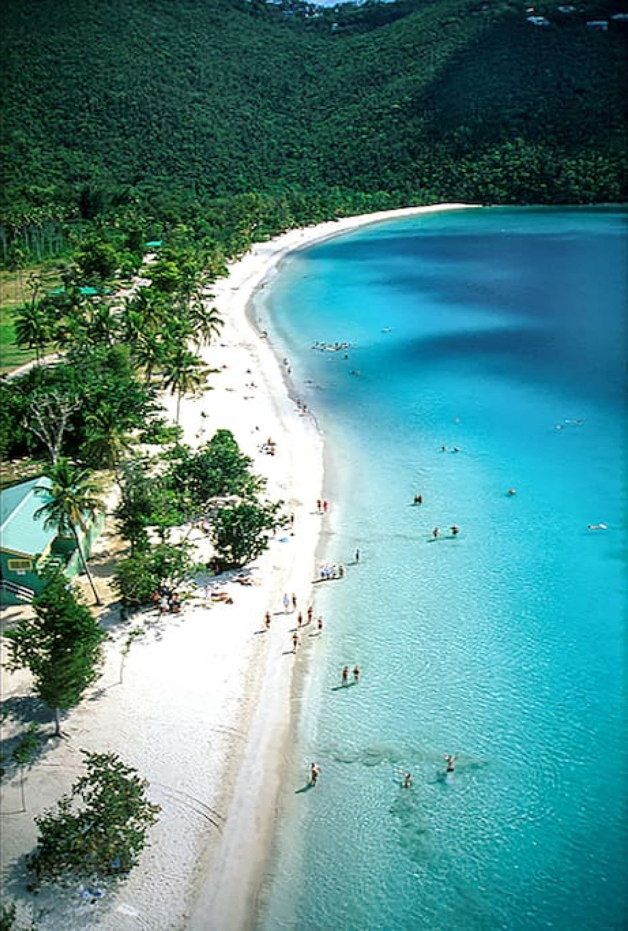 Une vue aérienne d’une plage aux eaux turquoise et limpides, au sable blanc et à la végétation luxuriante.