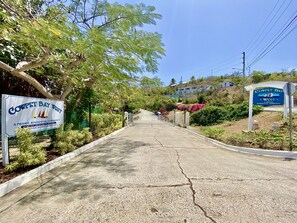 A residential community entrance with a sign for Cowpet Bay West, a gated driveway, and surrounding greenery. - 2br on Cowpet Beach w/Huge pool & 2 restaurants! (St. Thomas)