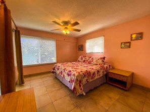 A bedroom with a bed, a ceiling fan, two windows with blinds, a nightstand, and a small cabinet. - 2BR just steps away from the beach and pool (St. Thomas)