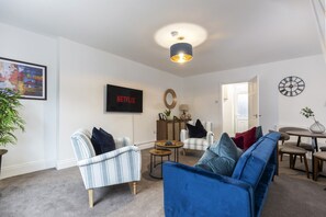 A living room with a sofa, armchairs, a coffee table, a television, and a clock on the wall. - The Cosy Pavilion: Stylish 2BR Home with Free Street Parking (Burnhope)
