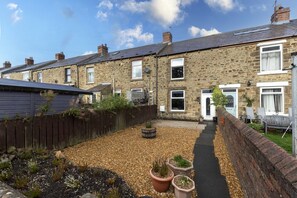 A stone house with a paved driveway, a wooden fence, and potted plants. - The Cosy Pavilion: Stylish 2BR Home with Free Street Parking (Burnhope)