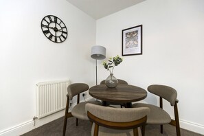 A dining area with a round table, four chairs, a wall clock, a floor lamp, and a framed picture. - The Cosy Pavilion: Stylish 2BR Home with Free Street Parking (Burnhope)