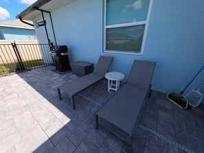 A patio with two lounge chairs, a small round table, and a grill.