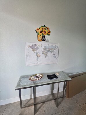 A wall-mounted world map, a small table with a decorative plate and a black notebook, and a wall decoration with sunflowers and a 'Welcome' sign.