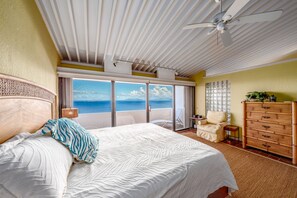Ein Schlafzimmer mit einem großen Bett, einem Deckenventilator, Meerblick, einem Sessel und einer Holzkommode.