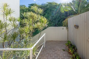 Ein Balkon mit Ziegelboden, umgeben von Topfpflanzen und einem weißen Geländer.