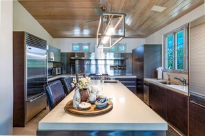 A modern kitchen with stainless steel appliances, a wooden ceiling, and a central island with a vase of flowers. - Vessup View · 5BR -Walk to the beach! Close to the Ritz Carlton! (St. Thomas)