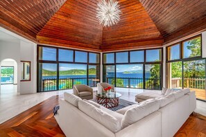 A spacious living room with a large white sofa, a coffee table, and a view of the sea through expansive windows. - 5BR Private Villa, Huge Pool, Ocean Views (St. Thomas)