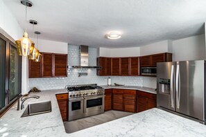 A modern kitchen with a gas stove, stainless steel appliances, wooden cabinets, and a marble countertop. - 5BR Private Villa, Huge Pool, Ocean Views (St. Thomas)