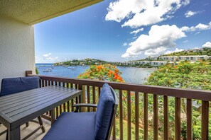 A balcony with a table and chairs, overlooking a coastal area with boats and buildings. - GORGEOUS 2BR Condo on the beach! Newly remodeled, sleeps 6. (St. Thomas)