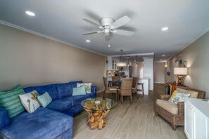 A living room with a blue sofa, a glass coffee table, wicker chairs, and a ceiling fan. - GORGEOUS 2BR Condo on the beach! Newly remodeled, sleeps 6. (St. Thomas)
