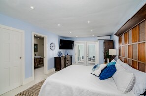 Une chambre avec un grand lit, un téléviseur fixé au mur, une armoire en bois et une porte donnant sur un balcon.