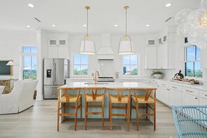 A spacious kitchen with white cabinetry, a central island with bar stools, and pendant lighting. - CSB~Ovation~5 BR Luxury Home~Beach, Bay, Pools Access~Panoramic Gulf & Bay Views (Port St. Joe)