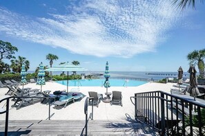 A poolside area with lounge chairs, umbrellas, and a view of the ocean. - CSB~Ovation~5 BR Luxury Home~Beach, Bay, Pools Access~Panoramic Gulf & Bay Views (Port St. Joe)