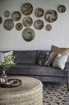 A living room with a grey sofa, a woven ottoman, and a wall decorated with circular woven art pieces. - 4br w/Incredible views of St. John and the BVI - sleeps 10 (St. Thomas)
