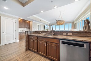 A modern kitchen with a central island, wooden cabinets, and a large window offering a view. - Phoenix OB II #801 -- Luxury 4BR Beachfront Corner Unit, VIEWS, Lazy  River (Orange Beach)