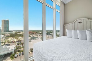 Een hotelkamer met een groot bed, uitzicht op een stadsgezicht en een balkon met palmbomen.