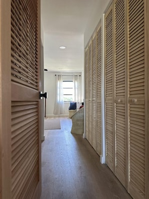 A hallway with wooden sliding doors, a bed with a white headboard, and a window with sheer curtains. - Dual Sapphire Beach Condos w/ Pool (St. Thomas)