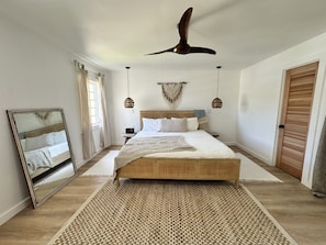A bedroom with a large bed, a ceiling fan, a mirror, and a wooden door. - Dual Sapphire Beach Condos w/ Pool (St. Thomas)