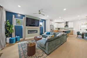 A modern living room with a sofa, a fireplace, and a kitchen in the background. - Emerald Oasis | Hot Tub | Game Room | Sleeps 12 (Columbus)