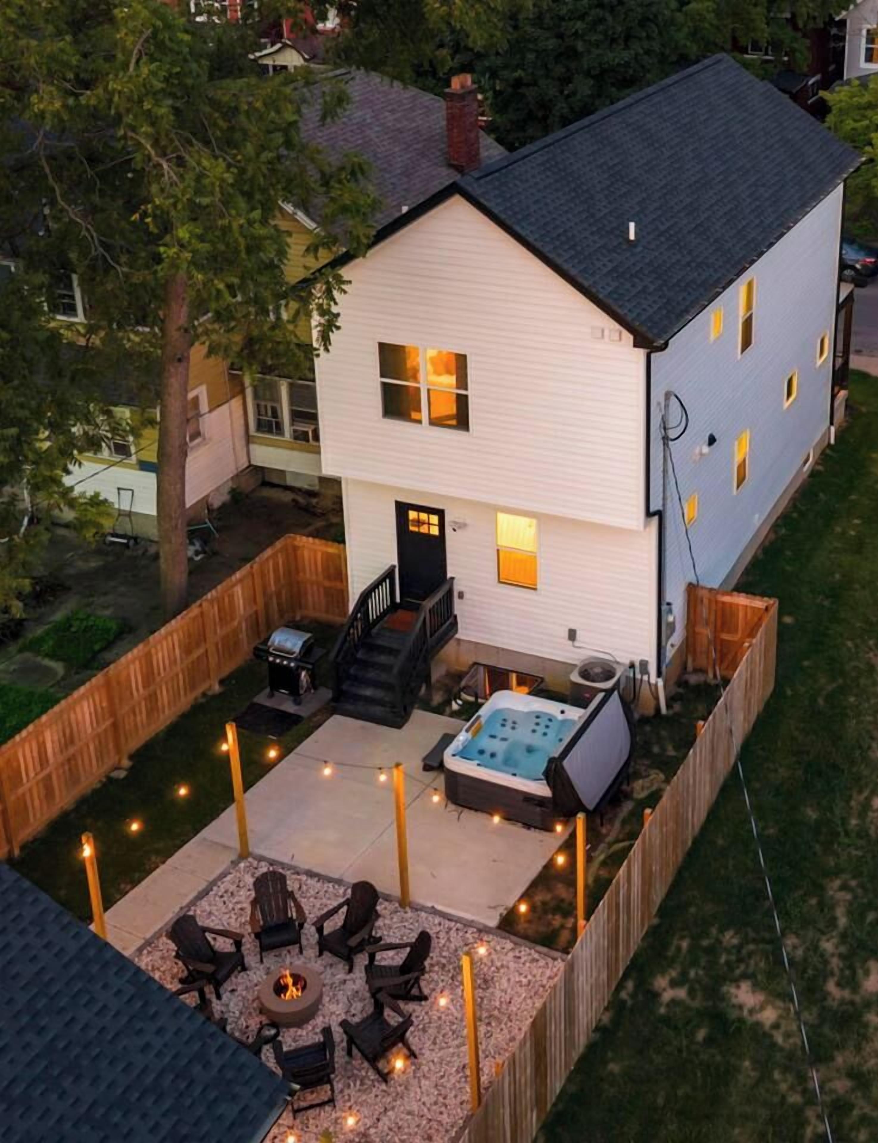 A two-story house with a fenced backyard, a hot tub, and outdoor seating.