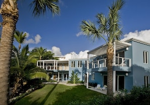 A two-story residential building with a balcony, surrounded by palm trees and a well-maintained lawn. - 5BR On Secret Harbor Beach - sleeps 14! (St. Thomas)