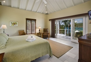 A bedroom with a bed, a chair, a desk, a lamp, a window, and a view of the outdoors. - 5BR On Secret Harbor Beach - sleeps 14! (St. Thomas)