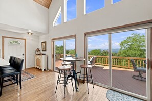 A spacious room with a wooden deck, large windows, and a dining area with a table and chairs.