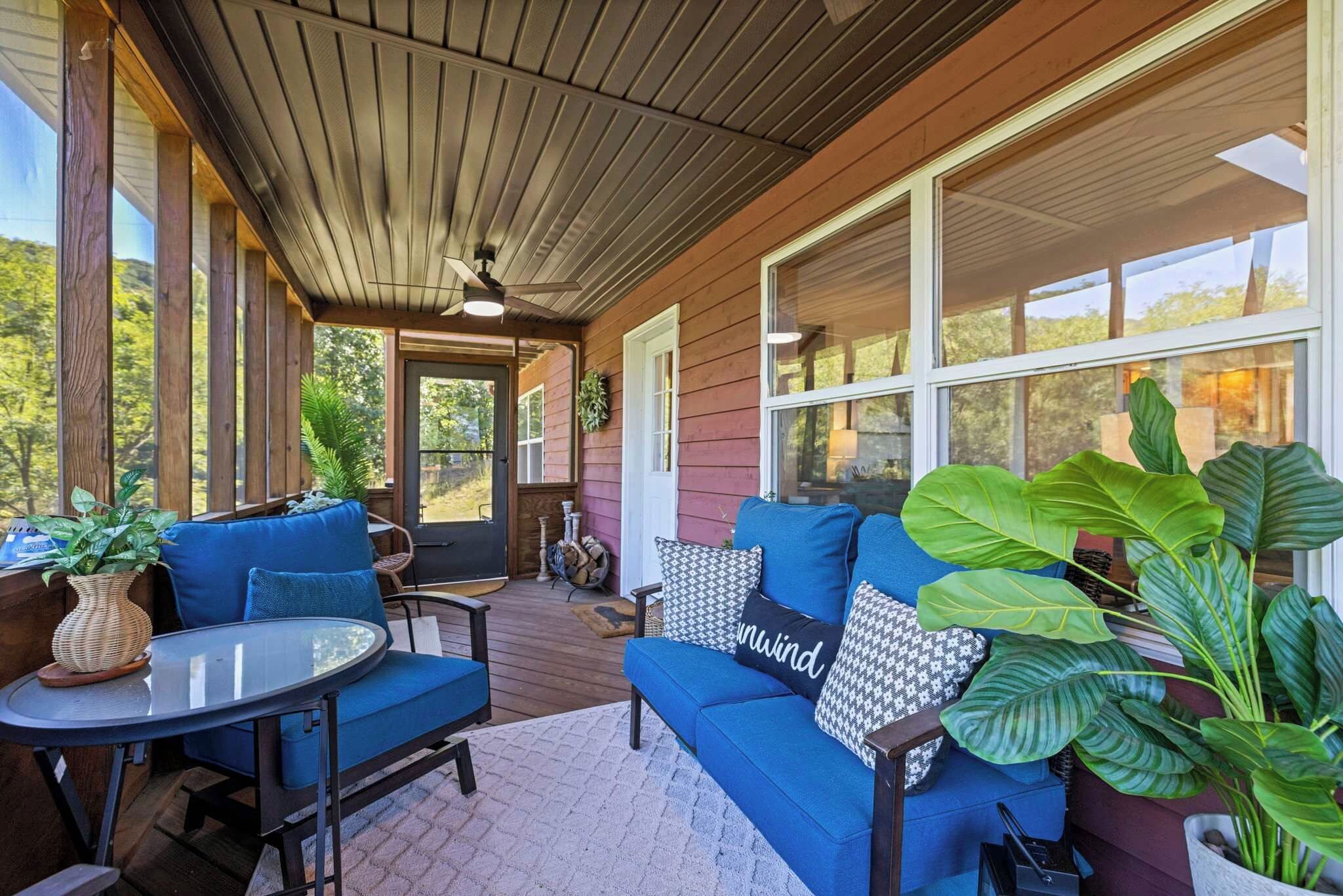 A covered porch with a blue sofa, a round table, and potted plants.