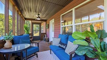 A covered porch with a blue sofa, a round table, and potted plants.