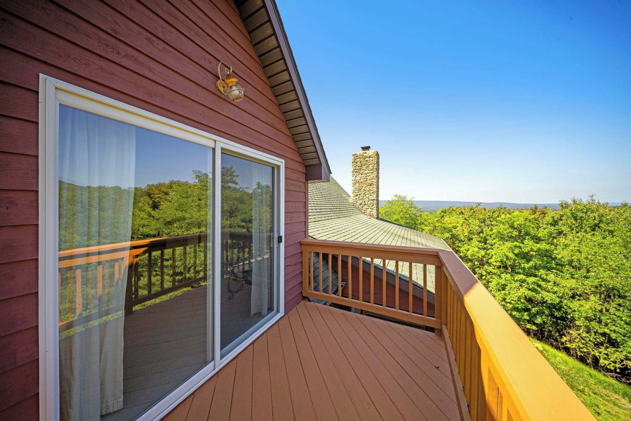 A wooden deck with a glass door leading to a balcony, overlooking a lush green landscape.