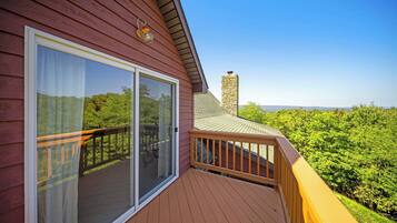 A wooden deck with a glass door leading to a balcony, overlooking a lush green landscape.