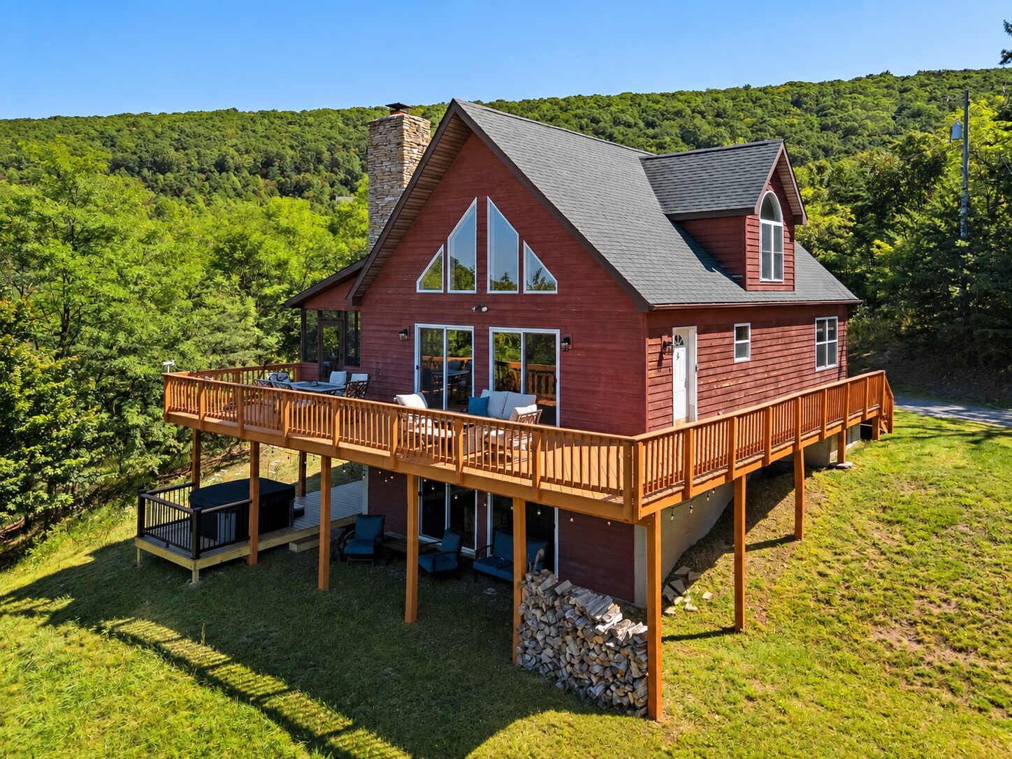 A red wooden house with a deck, large windows, and a stone chimney.