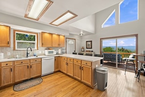 A modern kitchen with wooden cabinets, a dishwasher, and a dining area with a view.