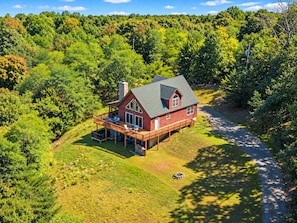 A red cabin with a large deck, surrounded by dense forest.