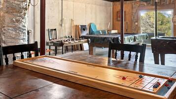 A room with a large wooden shuffleboard table, wooden chairs, and a foosball table.