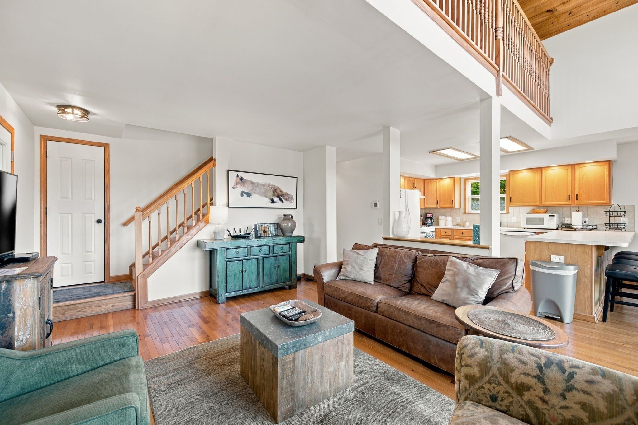 A spacious living room with a wooden staircase, a kitchen with wooden cabinets, and a dining area.