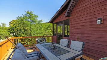 A wooden deck with a table and chairs, a door, and a view of trees.