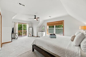 A bedroom with a large bed, a ceiling fan, a dresser, and a window with blinds.