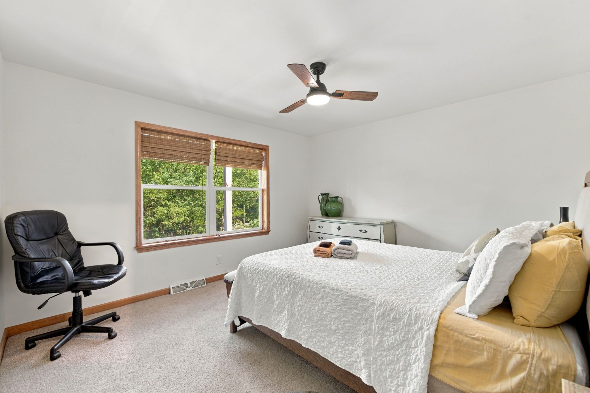 A bedroom with a bed, a desk, a chair, a window, and a ceiling fan.
