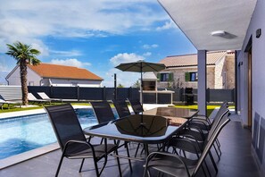 Eine Außenpatio mit Pool, einem Tisch mit Stühlen und Grillplatz.