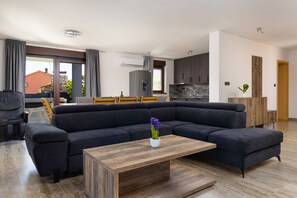 A modern living room with a sectional sofa, a wooden coffee table, and a dining area with chairs and a table. - Villa Azur – Modern Villa with a Swimming Pool and Jacuzzi on the Island of Krk (Hlapa (Krk))