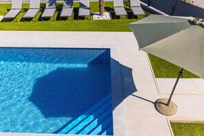 Piscina com água azul cristalina, cercada por um deck ladrilhado e área gramada com espreguiçadeiras.