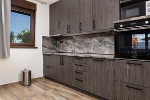 Uma cozinha com armários cinza, uma lixeira de aço inoxidável e um forno preto.