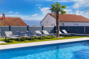 Ein Pool mit Liegestühlen und einer Palme, umgeben von einem Zaun und einem Gebäude mit einem Ziegeldach.